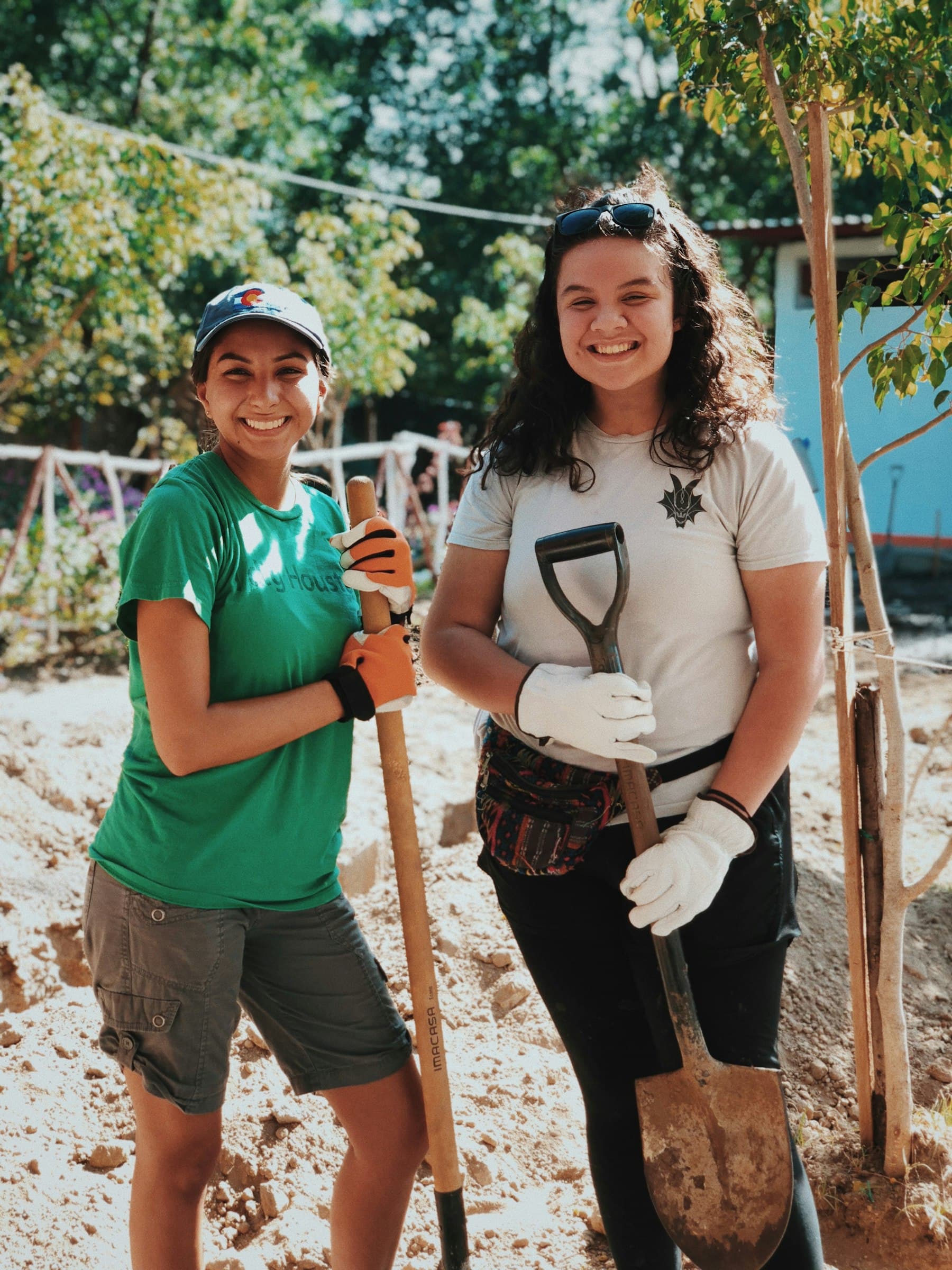 Two volunteers in gloves lean on shovels at a community planting day.